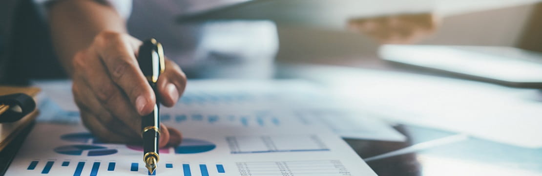 A man's hand holding a pen pointing at a paper graph. 